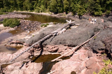 A remnant of the gray, 1.1 billion-year-old lava flow called the Keweenawan basalt, extruded during the Grenville Orogeny (mountain-building episode), covers the 2.7 billion-year-old pink granite next to the lower Chippewa Falls (hidden right rear).